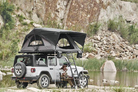 Roof Topper Tents on SUV parked by a lake with a person sitting underneath, enhancing the outdoor camping experience.
