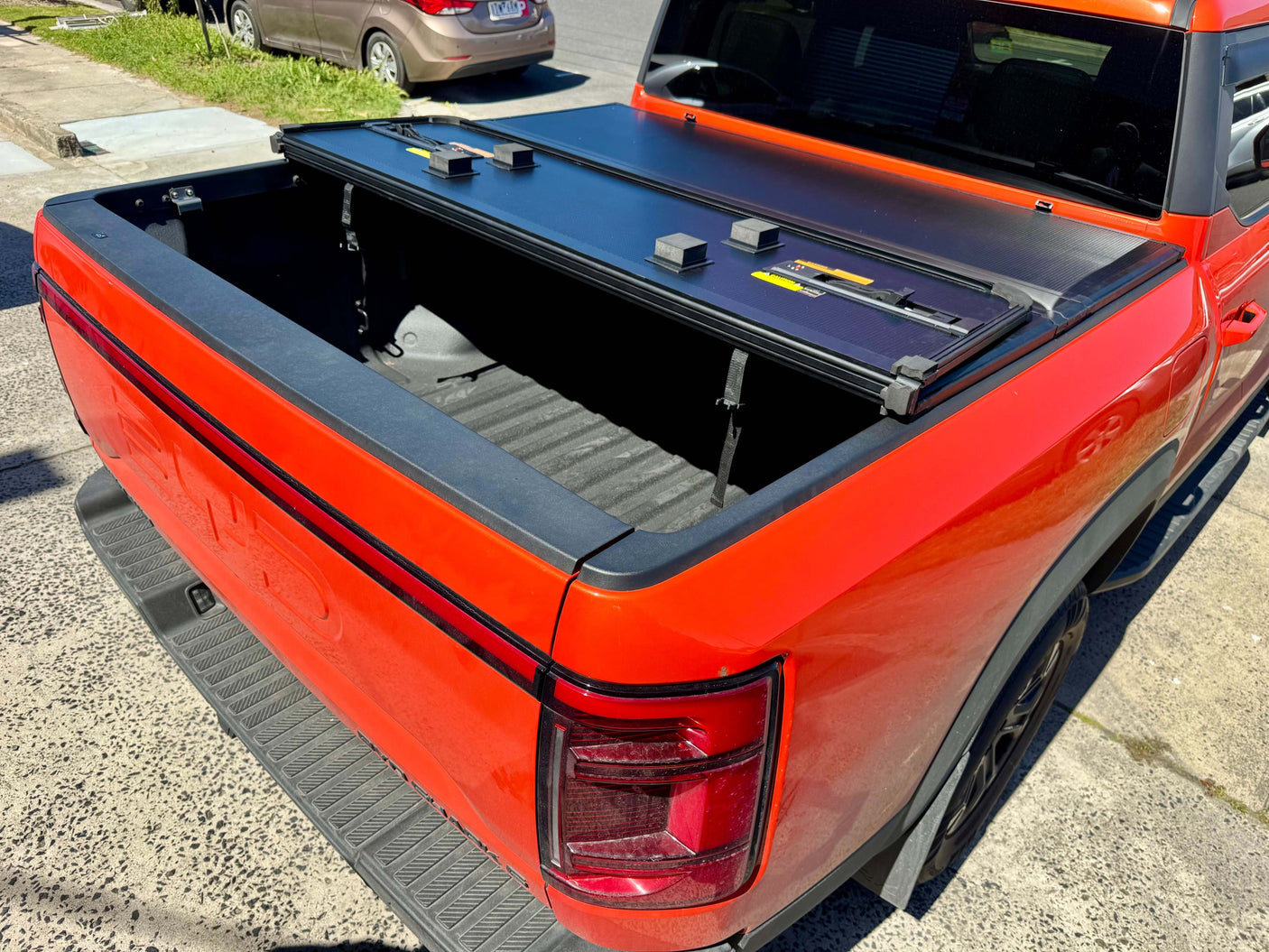 Red pickup truck with BYD Shark 6 hard lid tri-fold cover, open view showing secure tonneau design for 2025+ models