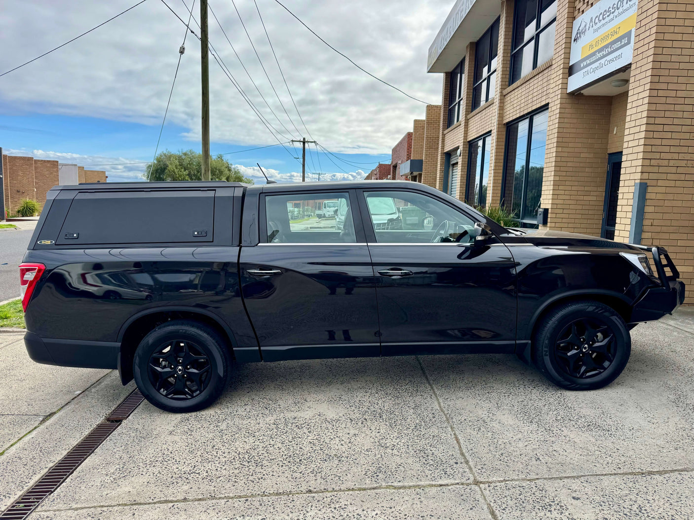 Black KGM Musso Canopy XLV 2018-2025 with stainless steel ute canopy parked outside an industrial building.