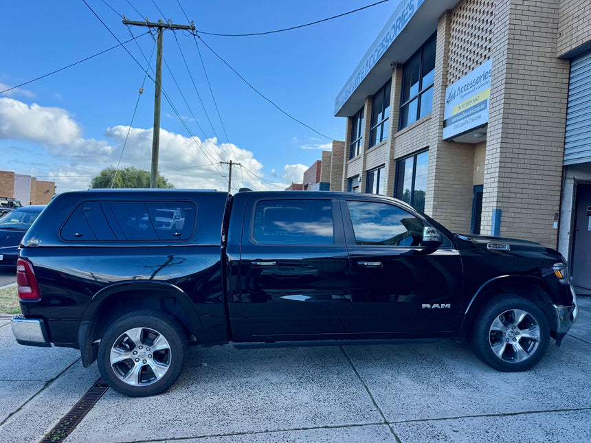 Black RAM 1500 canopy parked outside an industrial building, showcasing durability and style.