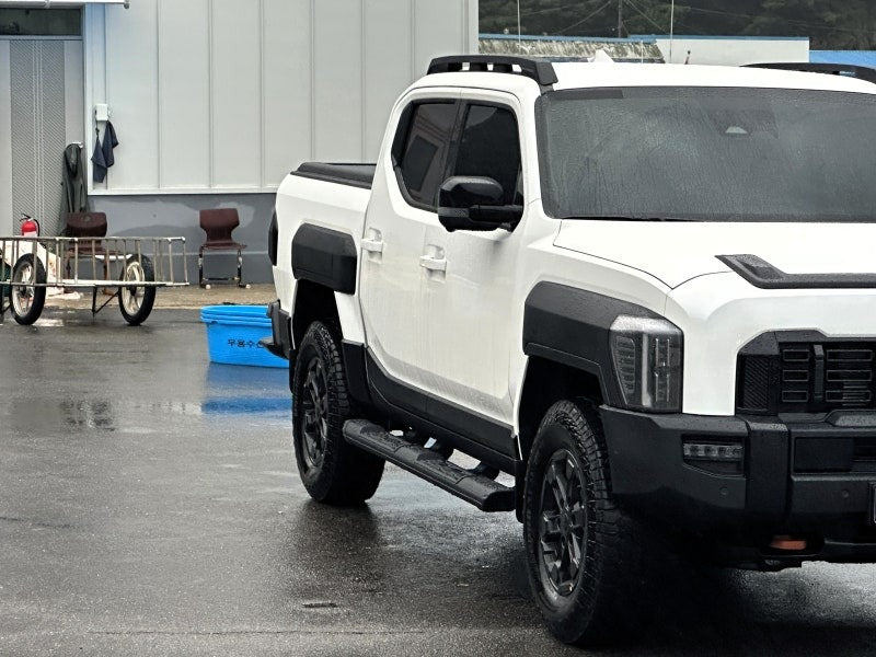 White 2025+ vehicle with Kia Tasman side steps, black steel side bars for strength and style, parked in a wet urban setting.