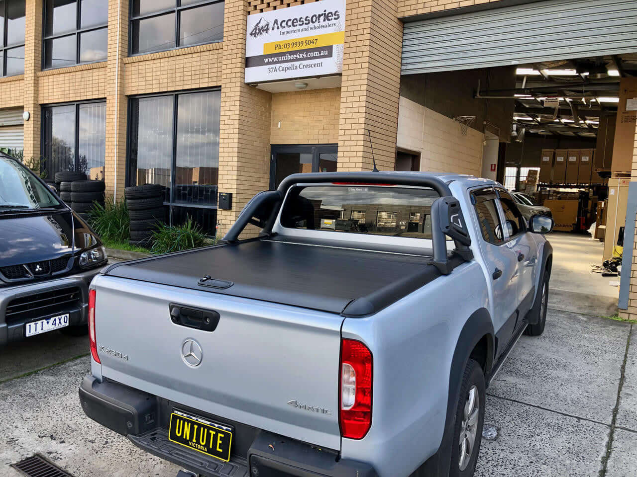 Mercedes-Benz X-Class 2017-2021 with UniUte Gen1 Manual x class roller shutter installed, parked in front of accessories shop.