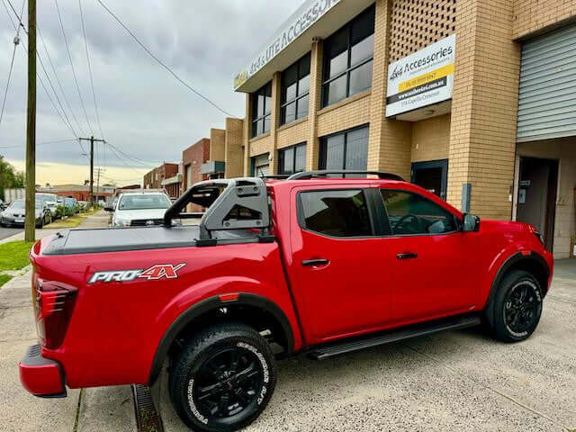 Red Nissan Navara with roller shutter for nissan navara installed, parked outside a building.