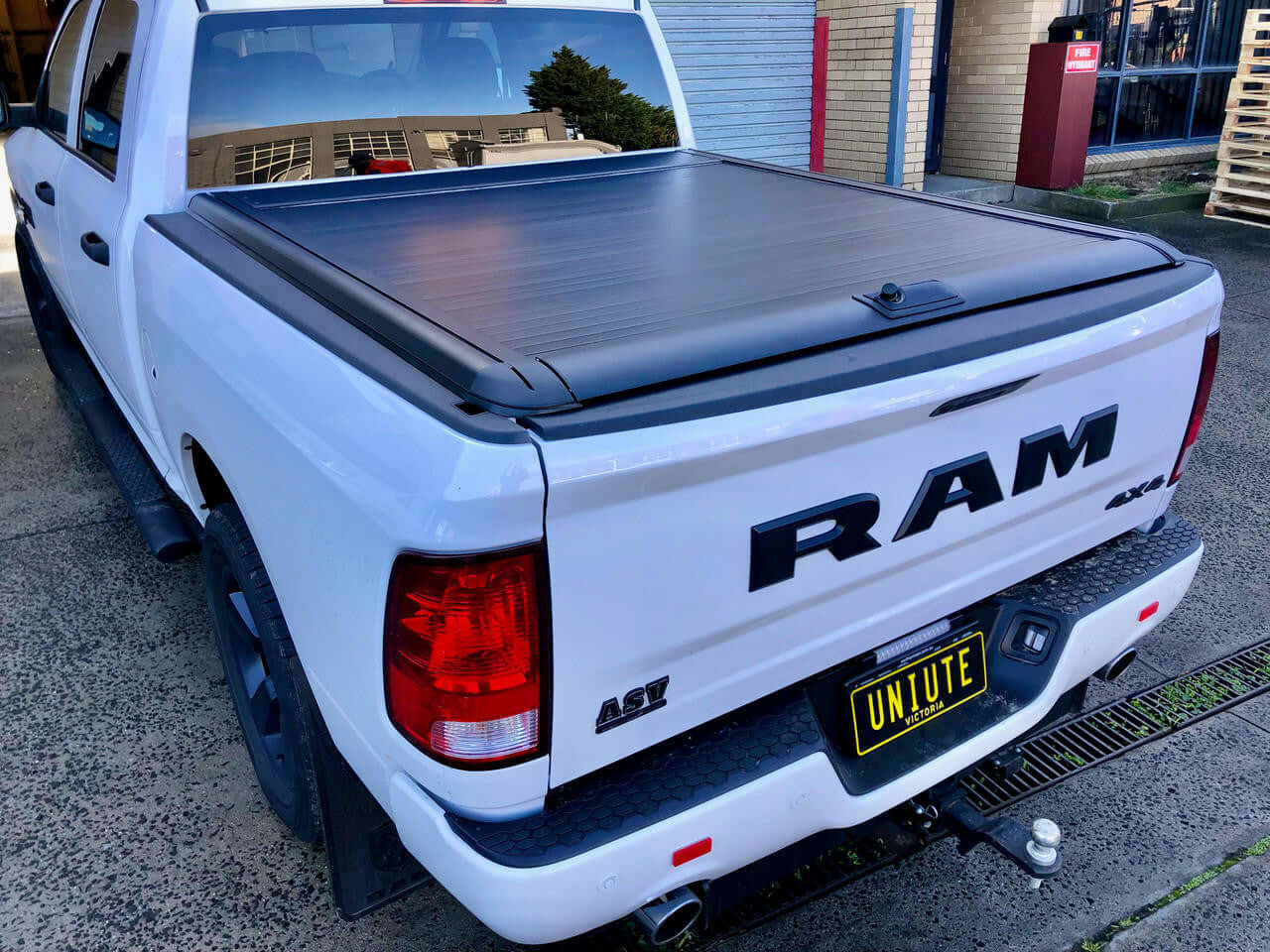 White truck with ram 1500 roller shutter covering the bed, parked outdoors.