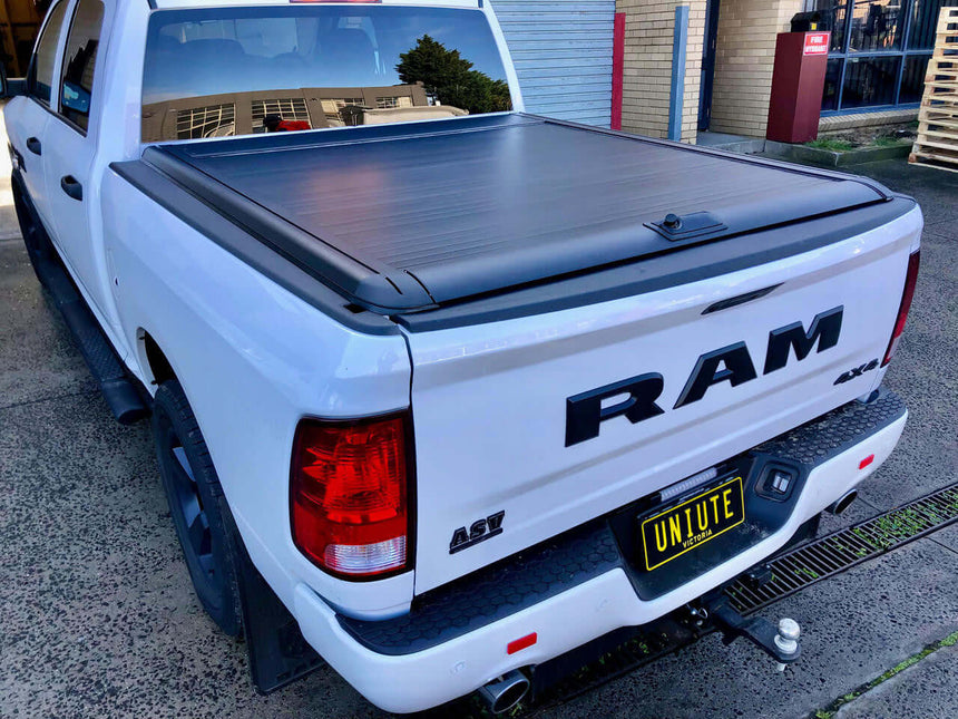 White truck with ram 1500 roller shutter covering the bed, parked outdoors.