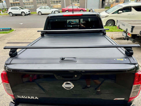 Black roller shutter racks cross bars for UniUte Gen2 roller shutters on a parked truck, showcasing durability and sleek design.
