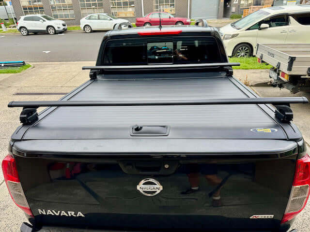 Black roller shutter racks cross bars for UniUte Gen2 roller shutters on a parked truck, showcasing durability and sleek design.