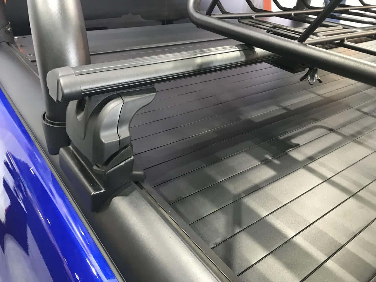 Close-up of roller shutter roof racks cross bars installed on a pickup truck, shown in sleek black aircraft-grade alloy.