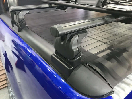 Close-up of roller shutter roof racks cross bars installed on a blue vehicle.