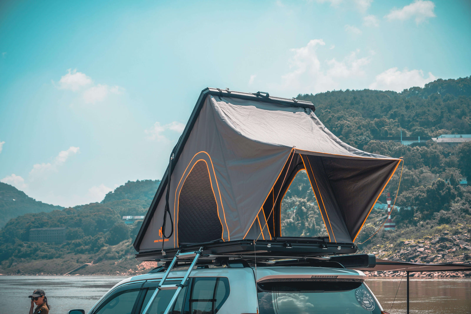 Hard Shell Rooftop Tent set up on a vehicle by a serene lakeside with mountains in the background, ideal for adventurous trips.