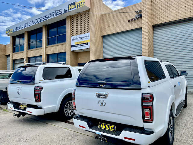 Two white utes with canopies parked outside an accessories store, highlighting Ute Canopy durability and functionality.