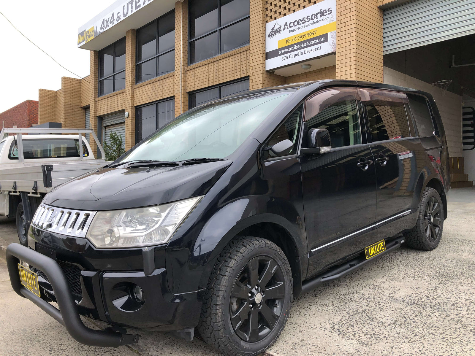 Black Mitsubishi Delica D5 parked in front of a 4x4 accessories shop, ready for adventure.