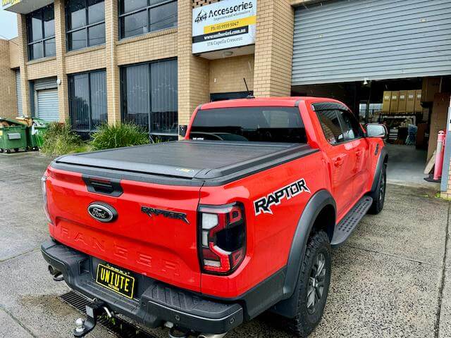 Red ute with roller shutters for utes installed, parked outside an auto accessories shop.