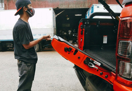 Person inspecting Amarok Tailgate Strut Kit on open vehicle in garage setting