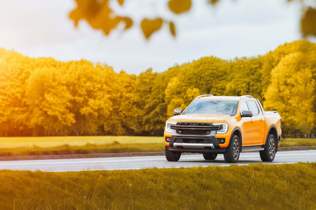 Yellow Ford Ranger truck driving on a road with surrounding trees, showcasing potential FORD RANGER ACCESSORIES for customization.