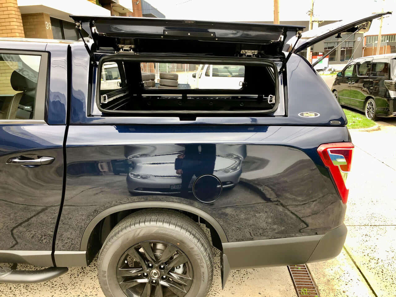SsangYong Musso XLV Canopy installed on a blue pickup truck, showcasing open rear hatch in an outdoor setting.